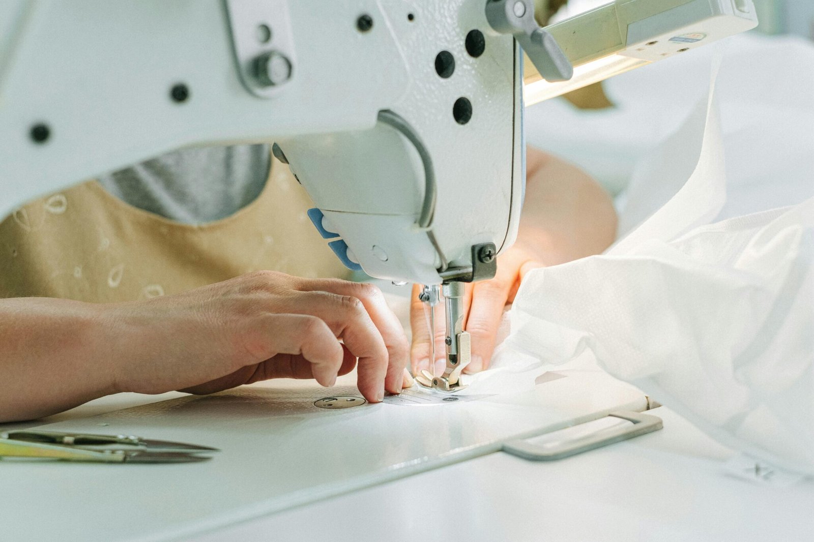 A seamstress using a sewing machine in a workshop, highlighting hands and fabric.